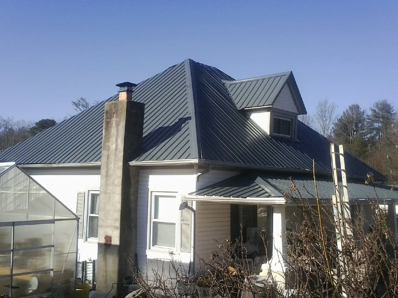 Dark blue standing seam metal roof on a white farmhouse with dormer — Slate & Tile Roof Repair by Roofing Brothers in Alexandria