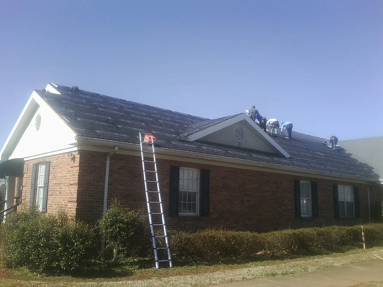 Crew tearing shingles off a brick ranch roof with a ladder set — Emergency Roof Repair work by our crew in Alexandria