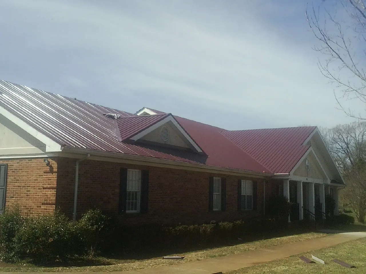 Red metal roof with gabled entries on a long brick building, from a Hail Damage Roof Repair job in Alexandria