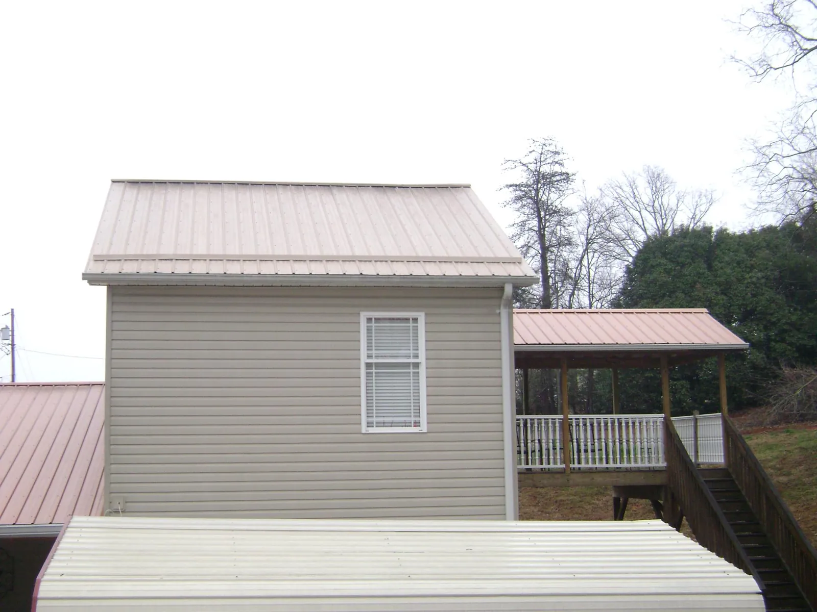 Tan metal roofs on a two story addition and attached porch, from a Roof Replacement job in Alexandria